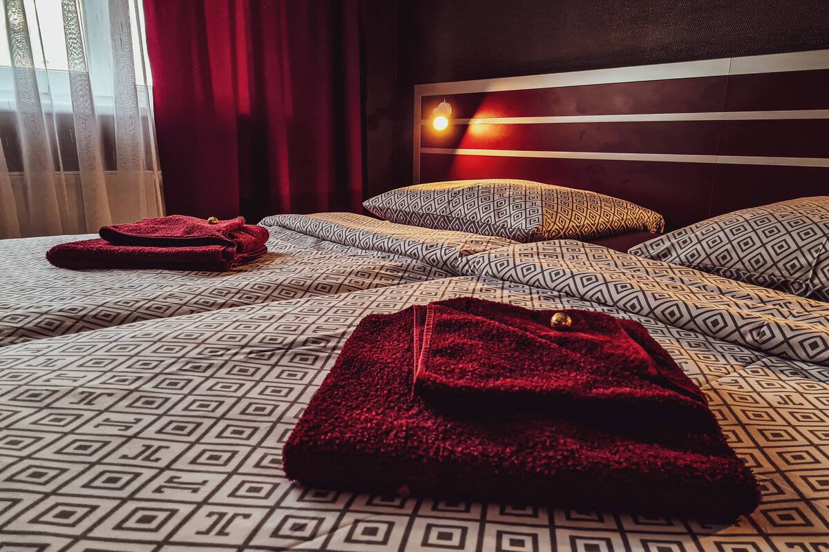 Quarto de hotel com colcha estampada, manta vermelha e cabeceira com luminária.