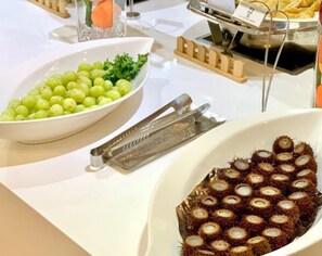 Ein Buffet mit einer Schüssel grüner Trauben, einer Speise in einem Teller mit Muster und einem Metallservierbesteck.