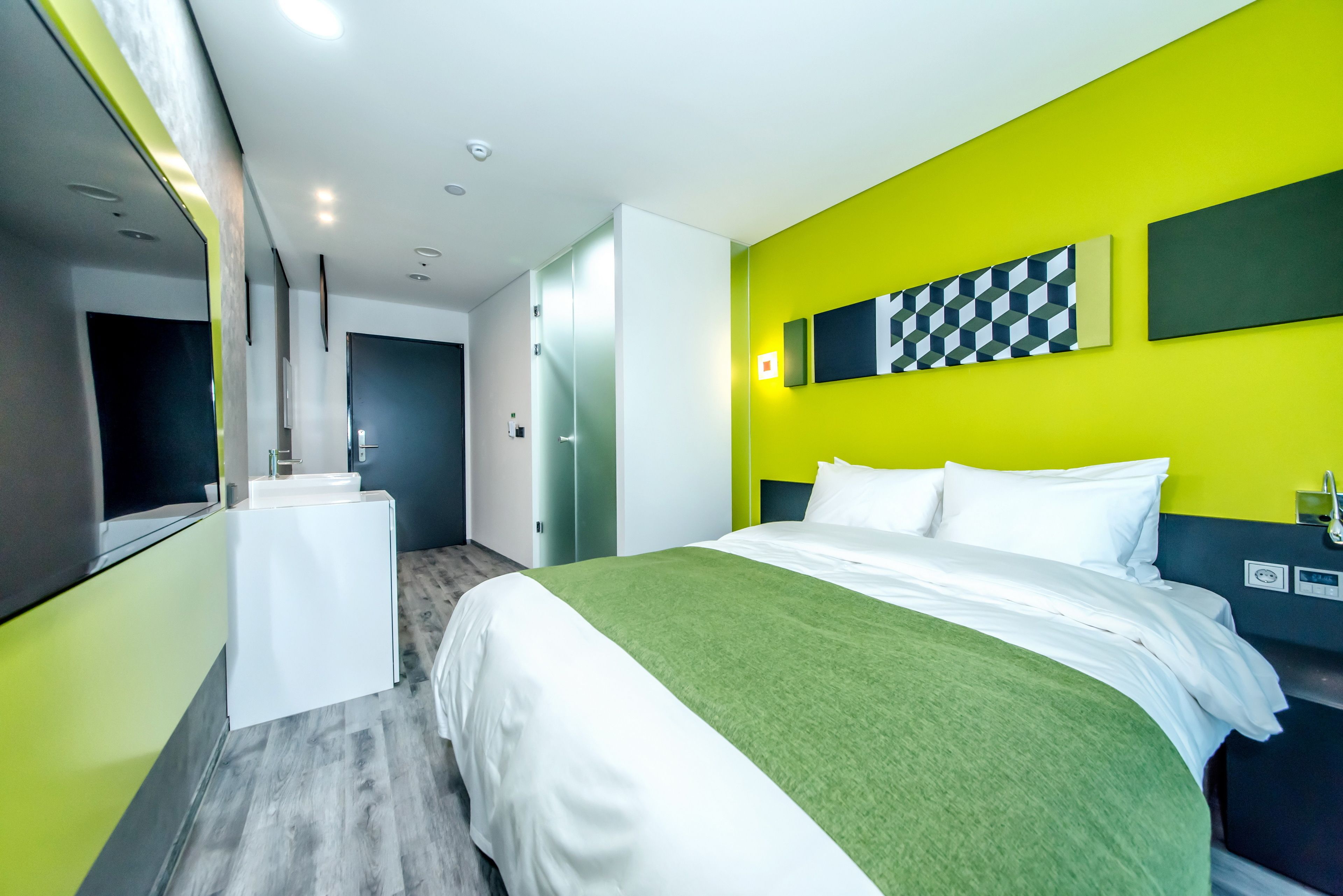 Una habitación de hotel moderna con una cama, un escritorio pequeño y una pared de color amarillo brillante.
