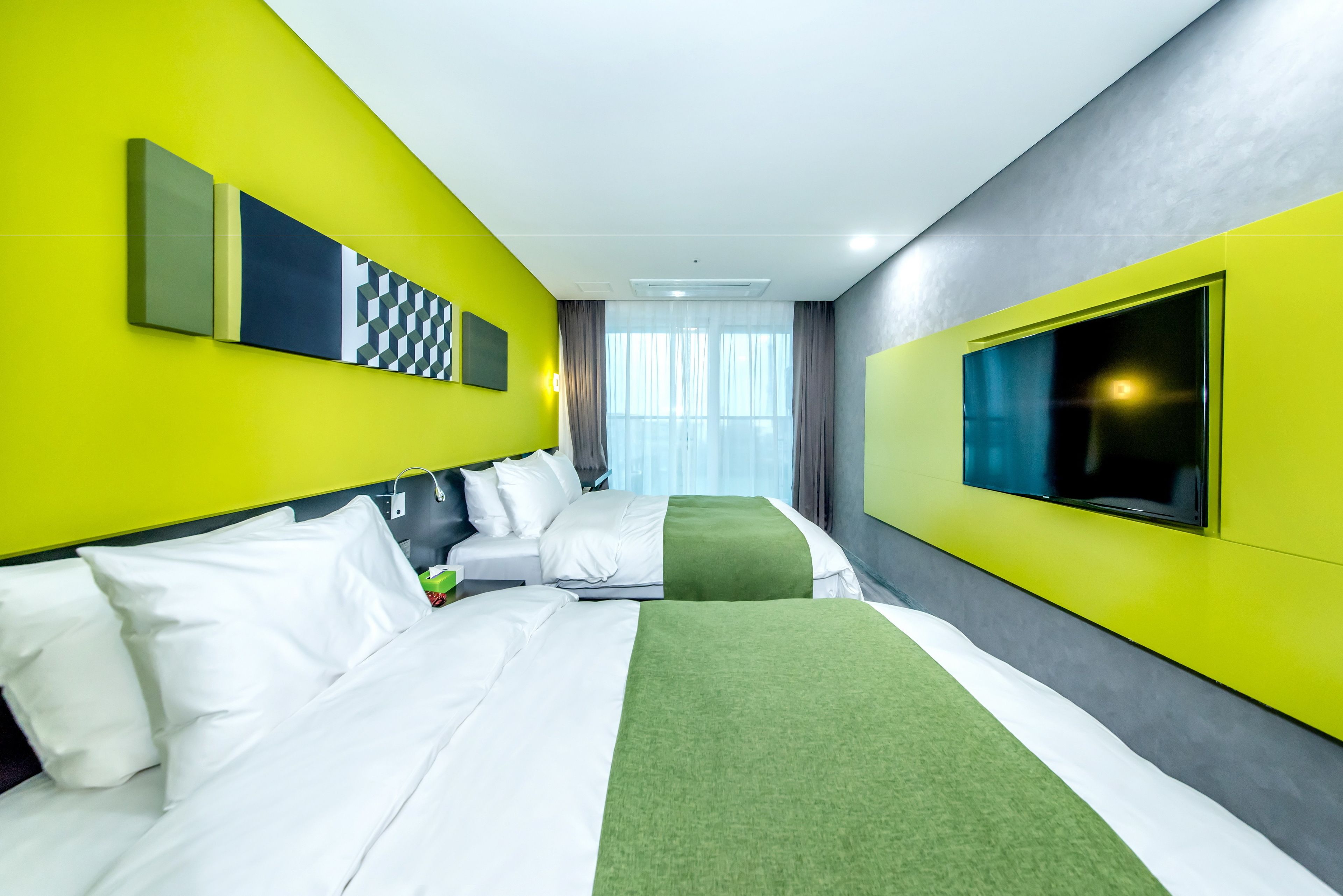 A hotel room with two beds, a large TV, and a bright yellow wall.