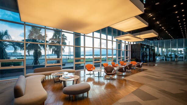 A modern lounge area with large windows, comfortable seating, and a view of the waterfront.