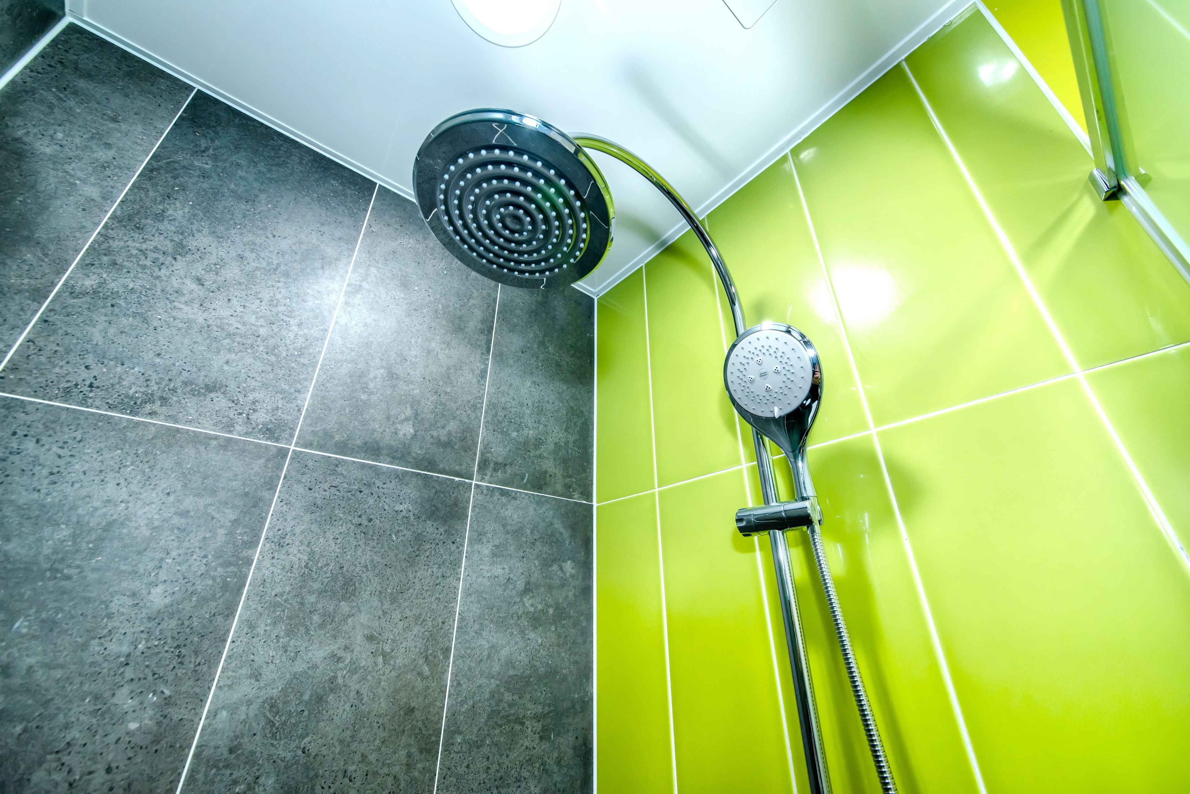 A shower area with a rain showerhead and a handheld showerhead, tiled floor, and a green wall.