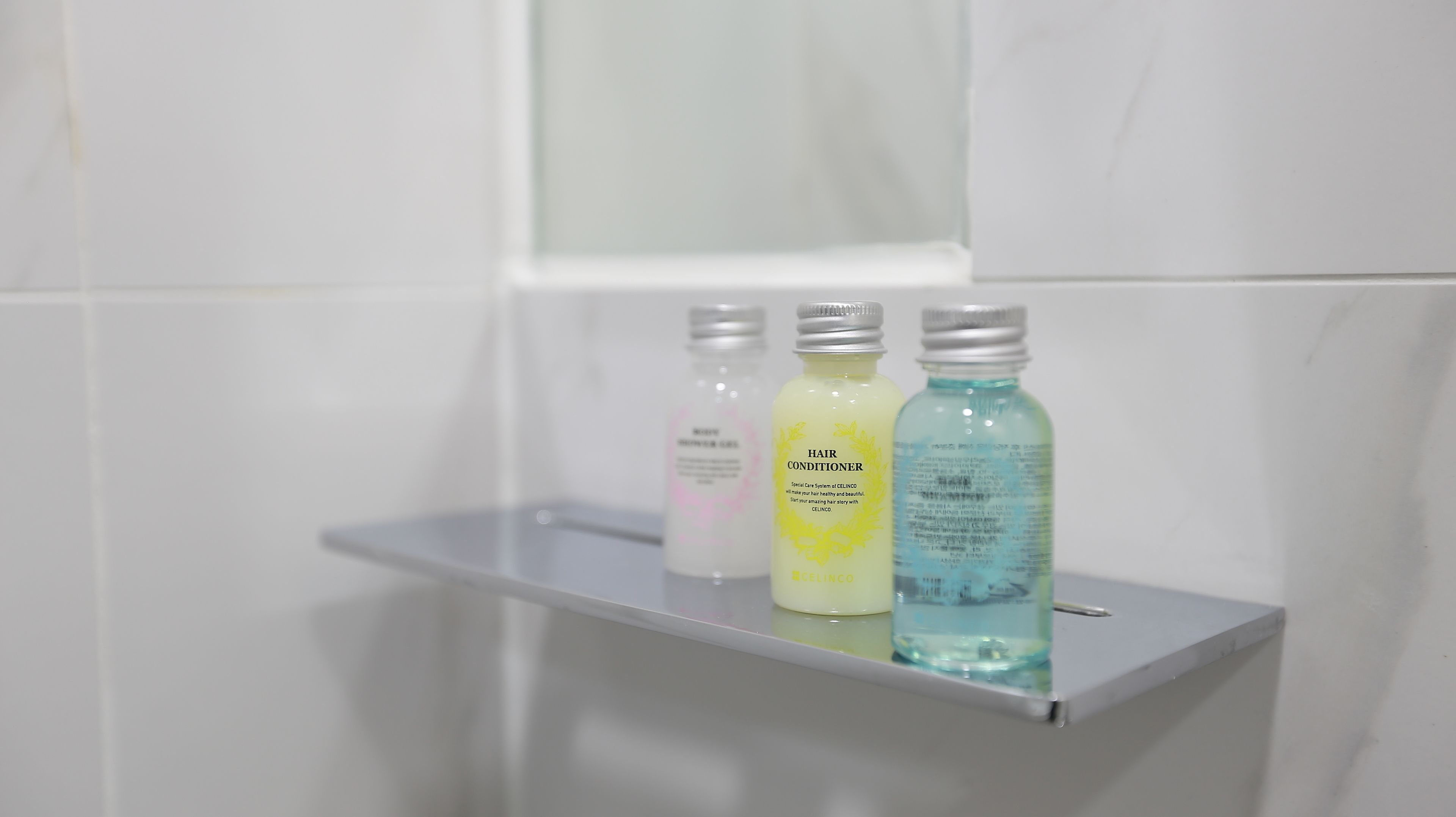 A bathroom shelf with three bottles of hair conditioner.