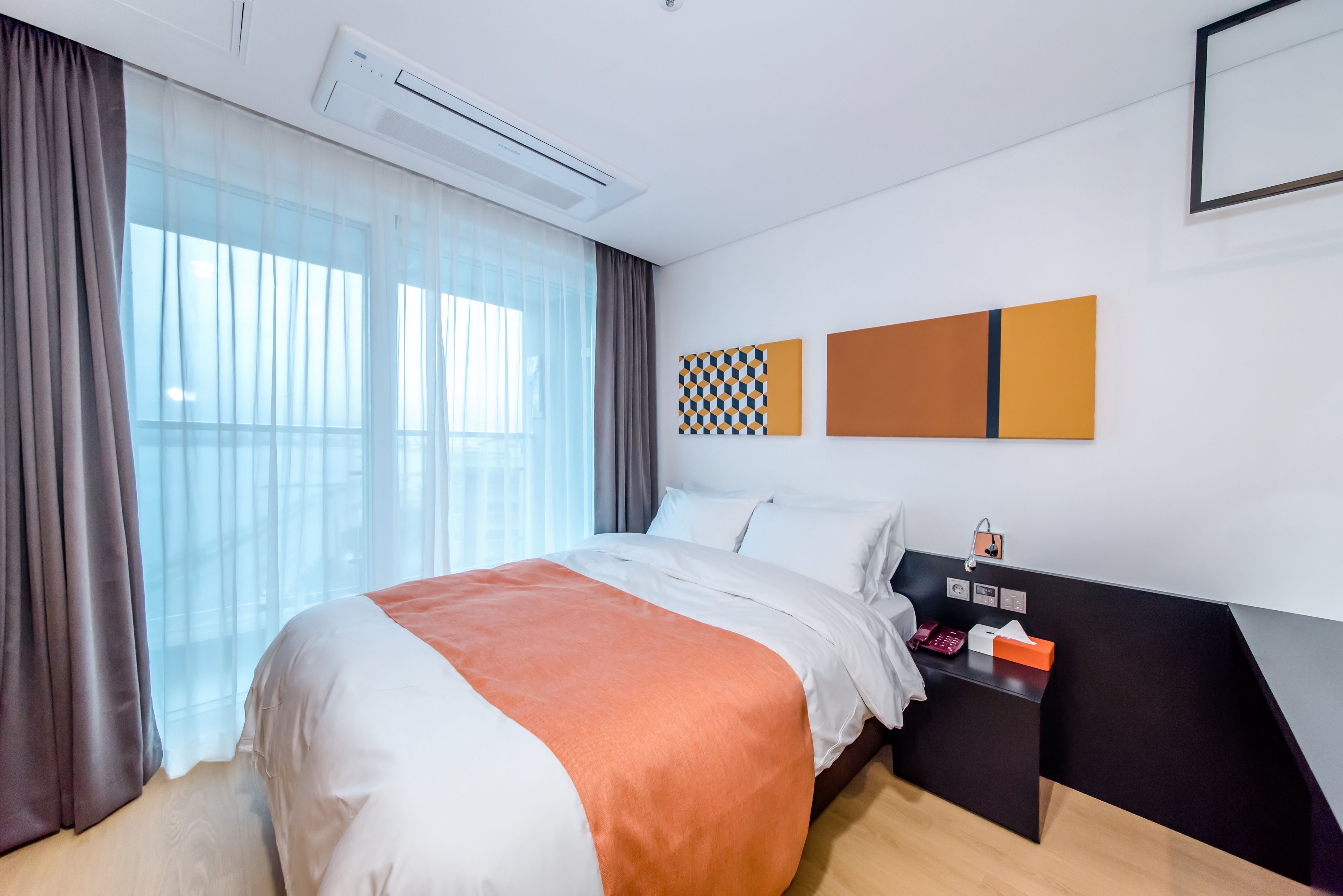 A modern hotel room with a large bed, a bedside table with a lamp, and a window with curtains.