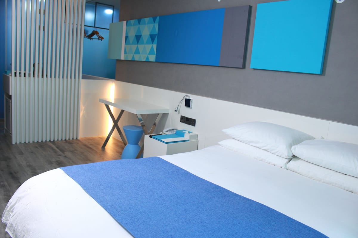 A modern hotel room with a large bed, a desk, and a chair.