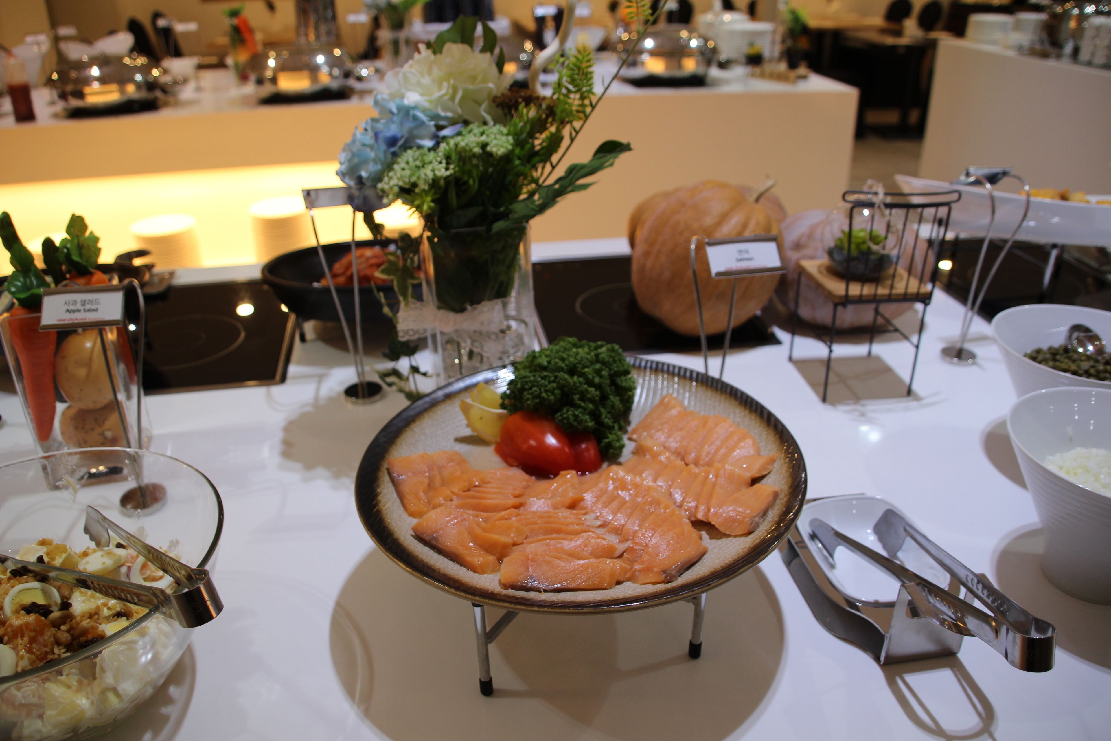 A buffet table with various food items, including salmon, vegetables, and a bowl of salad.