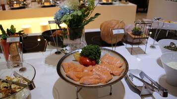 A buffet table with various food items, including salmon, vegetables, and a bowl of salad.