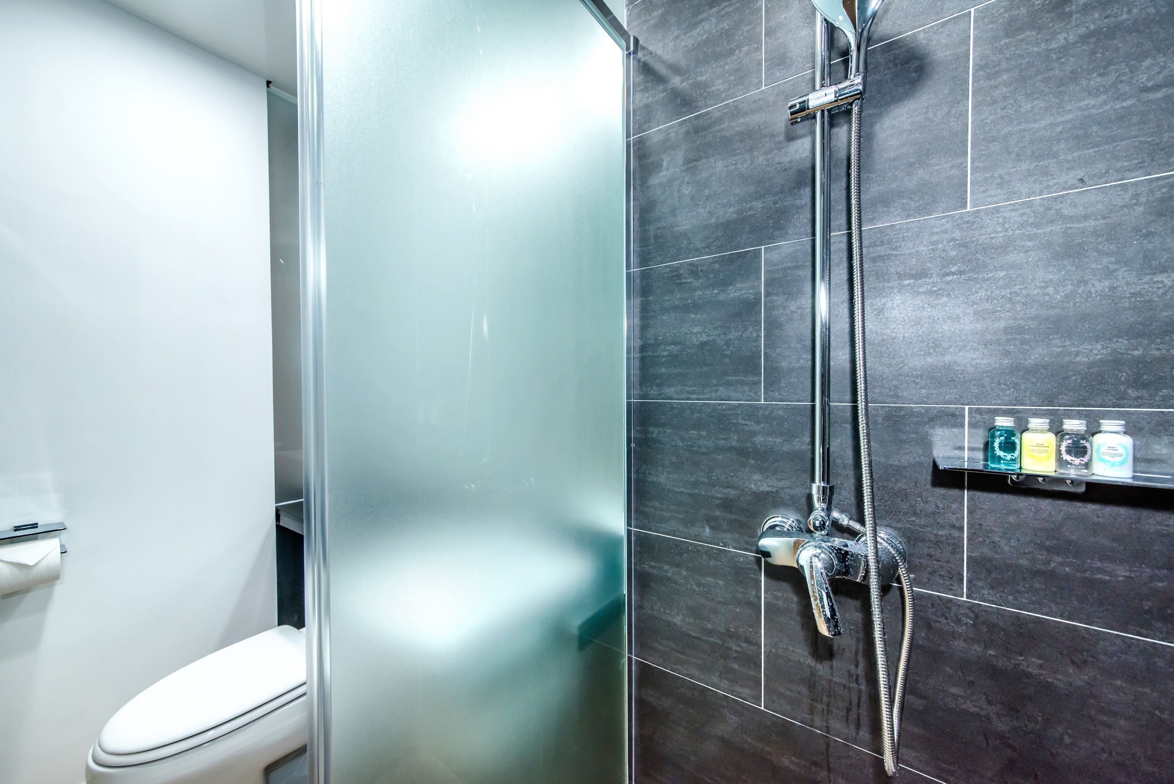 Une salle de bain avec une douche à parois de verre, des toilettes et une étagère contenant des articles de toilette.