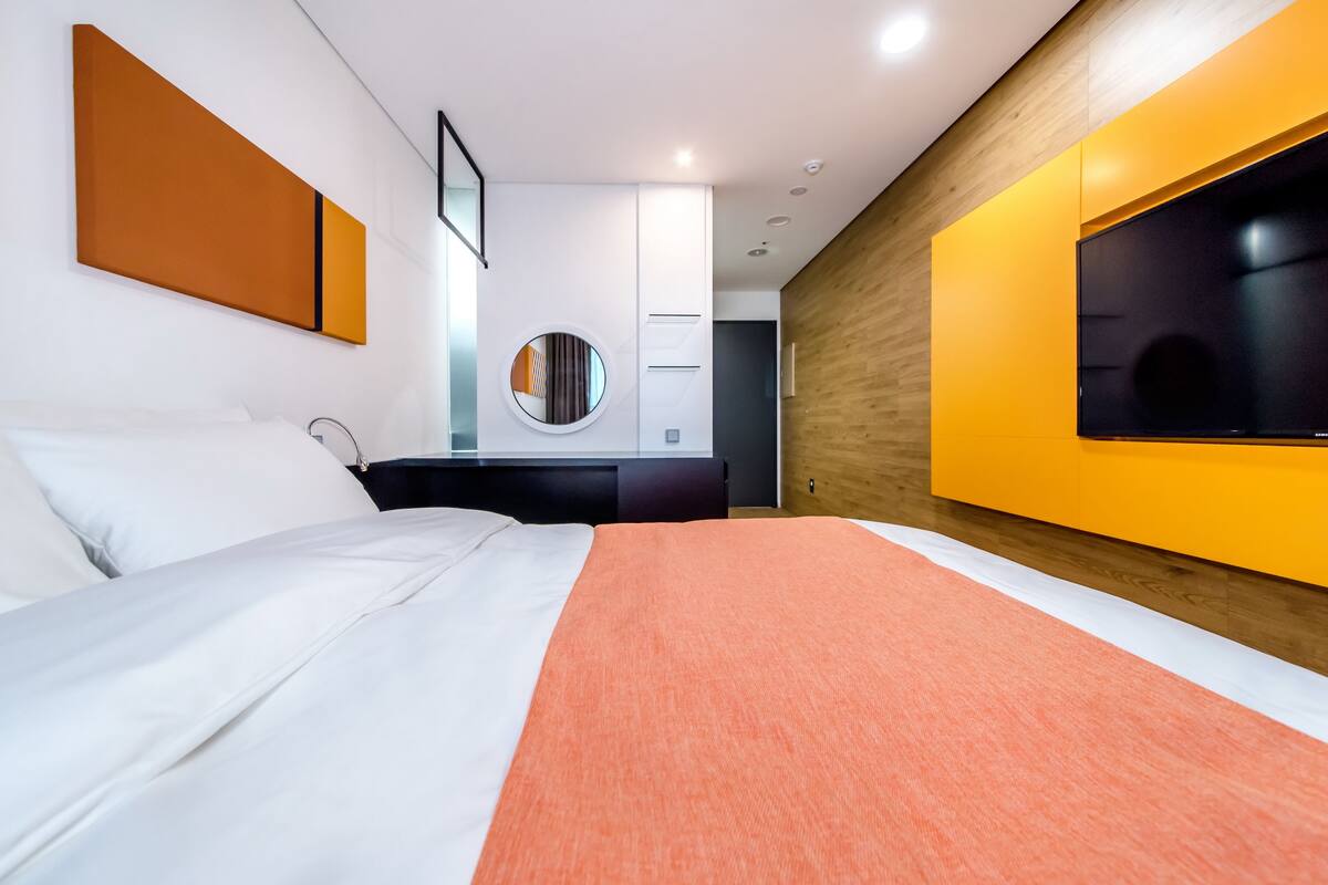 A modern hotel room with a large bed, a television mounted on the wall, and a wooden accent wall.