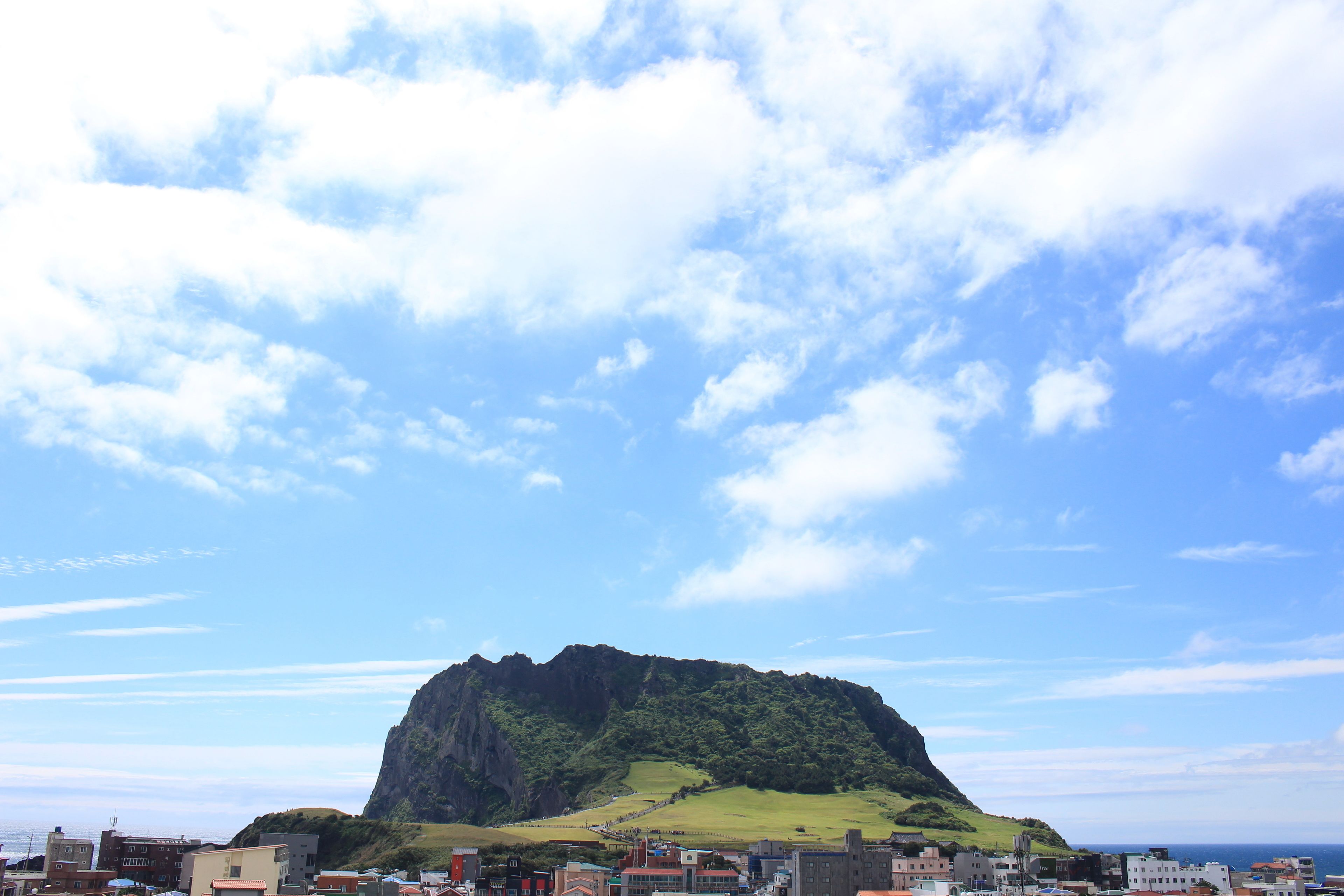 A coastal town with a prominent rocky hill in the background and a clear blue sky.