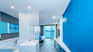 A modern hotel room with a large window, a bed, a white sink, and a blue accent wall.