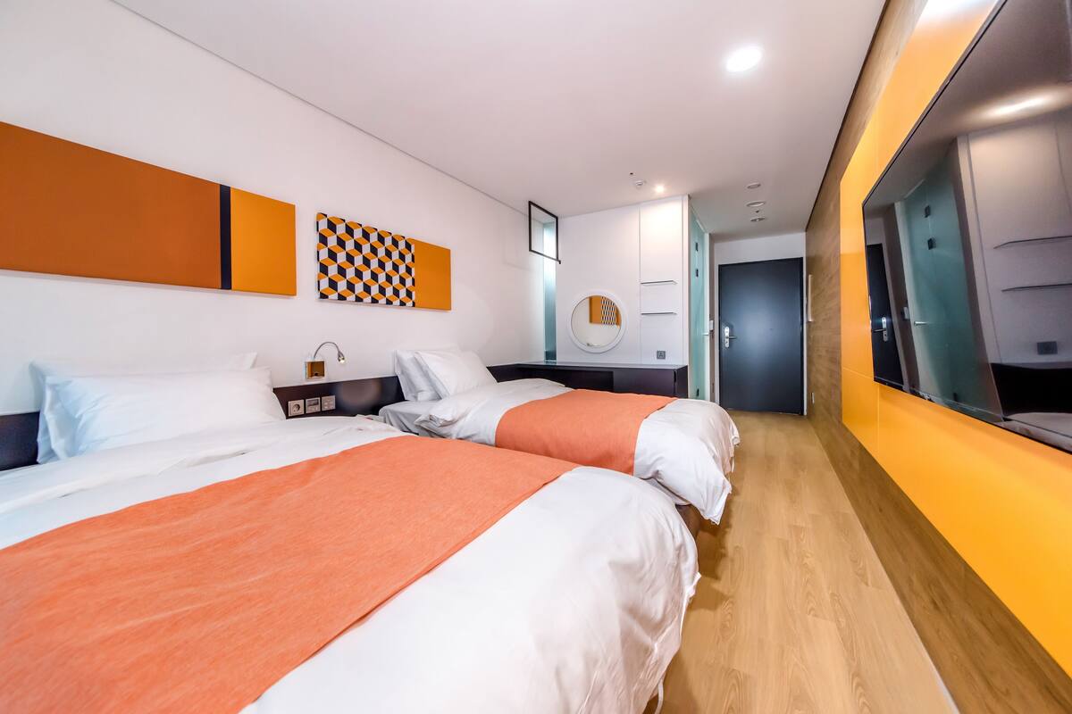 A modern hotel room with two beds, a large mirror, and a wooden floor.