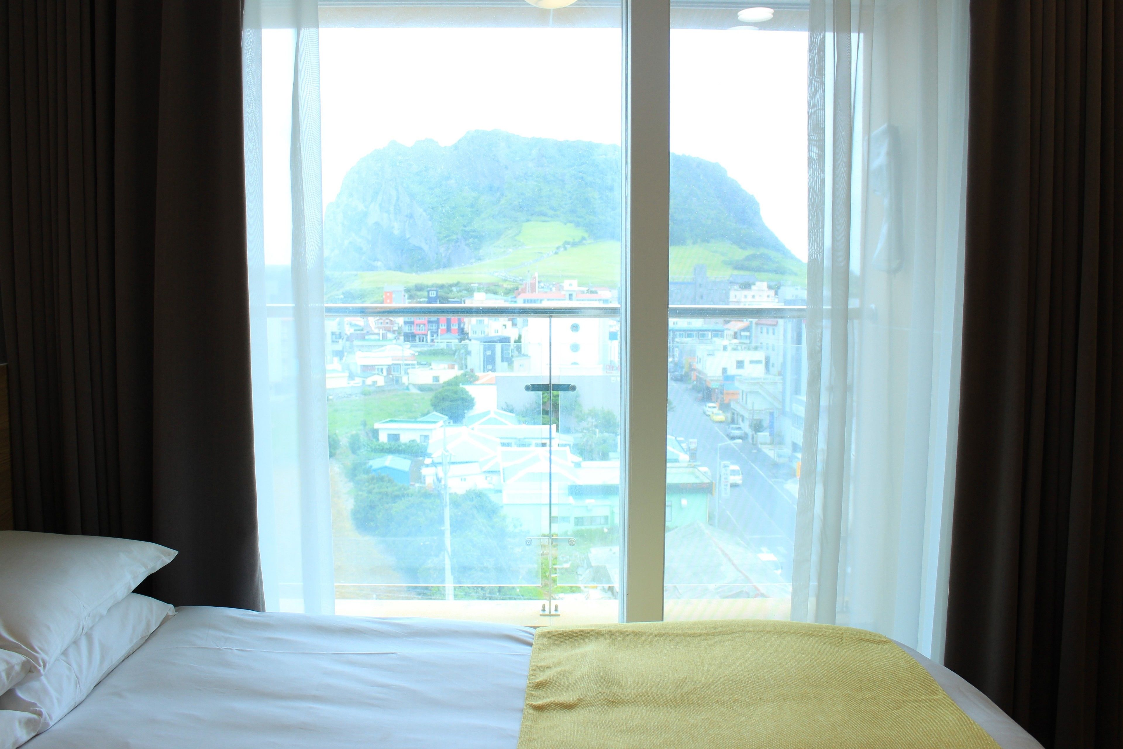 A hotel room with a large window offering a view of a mountainous landscape and a cityscape.