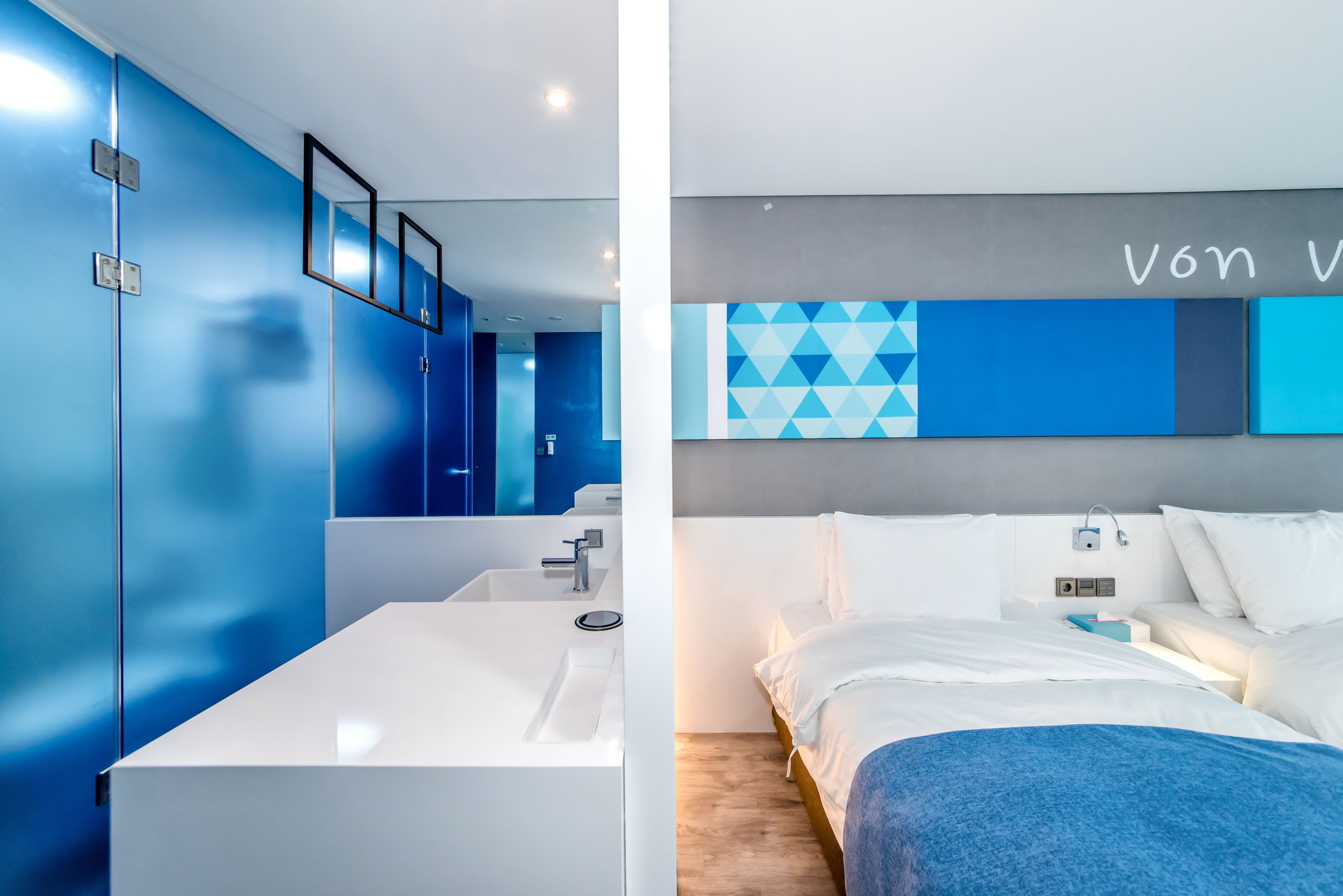 A modern hotel room with a large white sink, a bed with white bedding, and a blue accent wall.