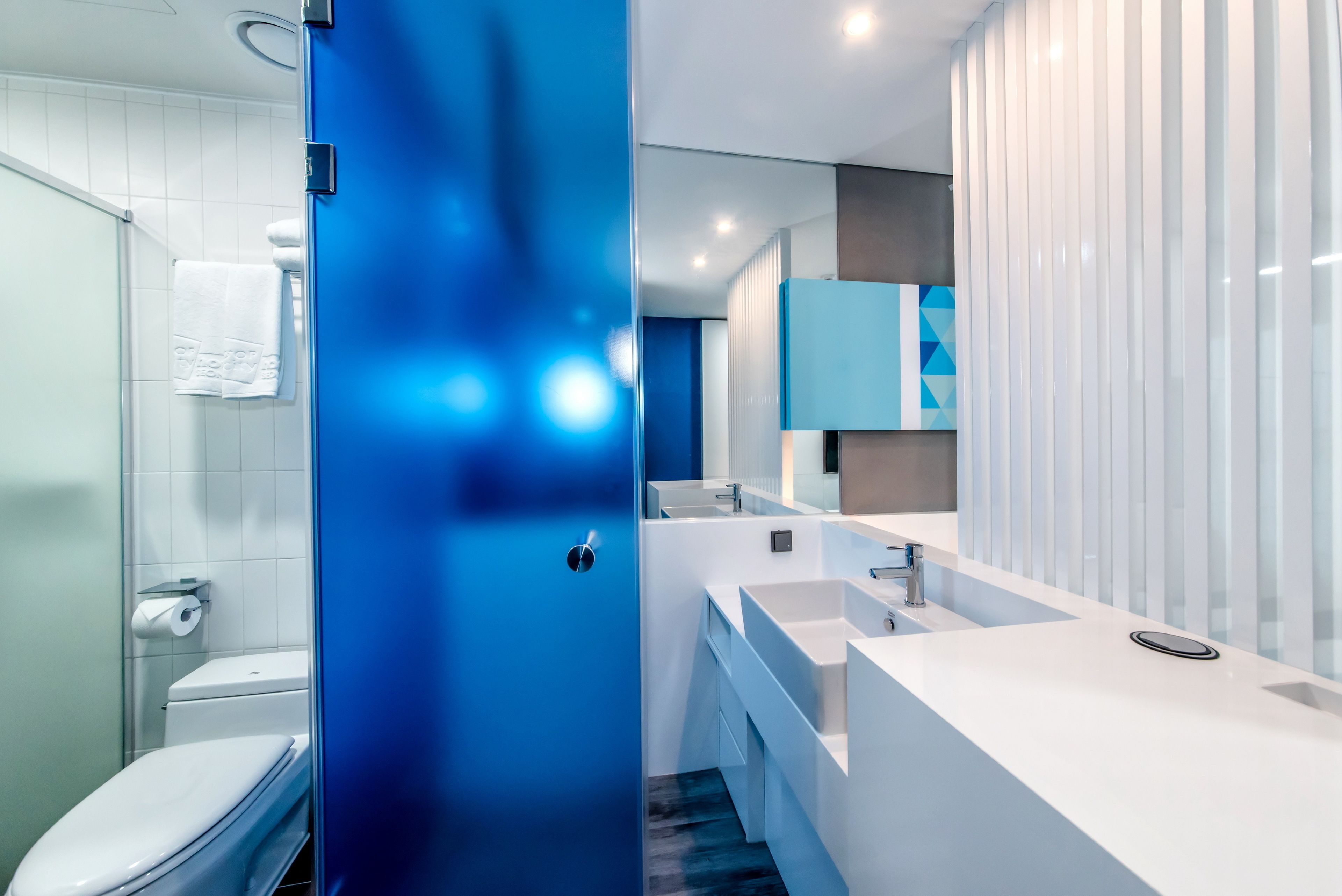 A modern bathroom with a white toilet, a blue accent wall, and a large sink with a mirror above it.