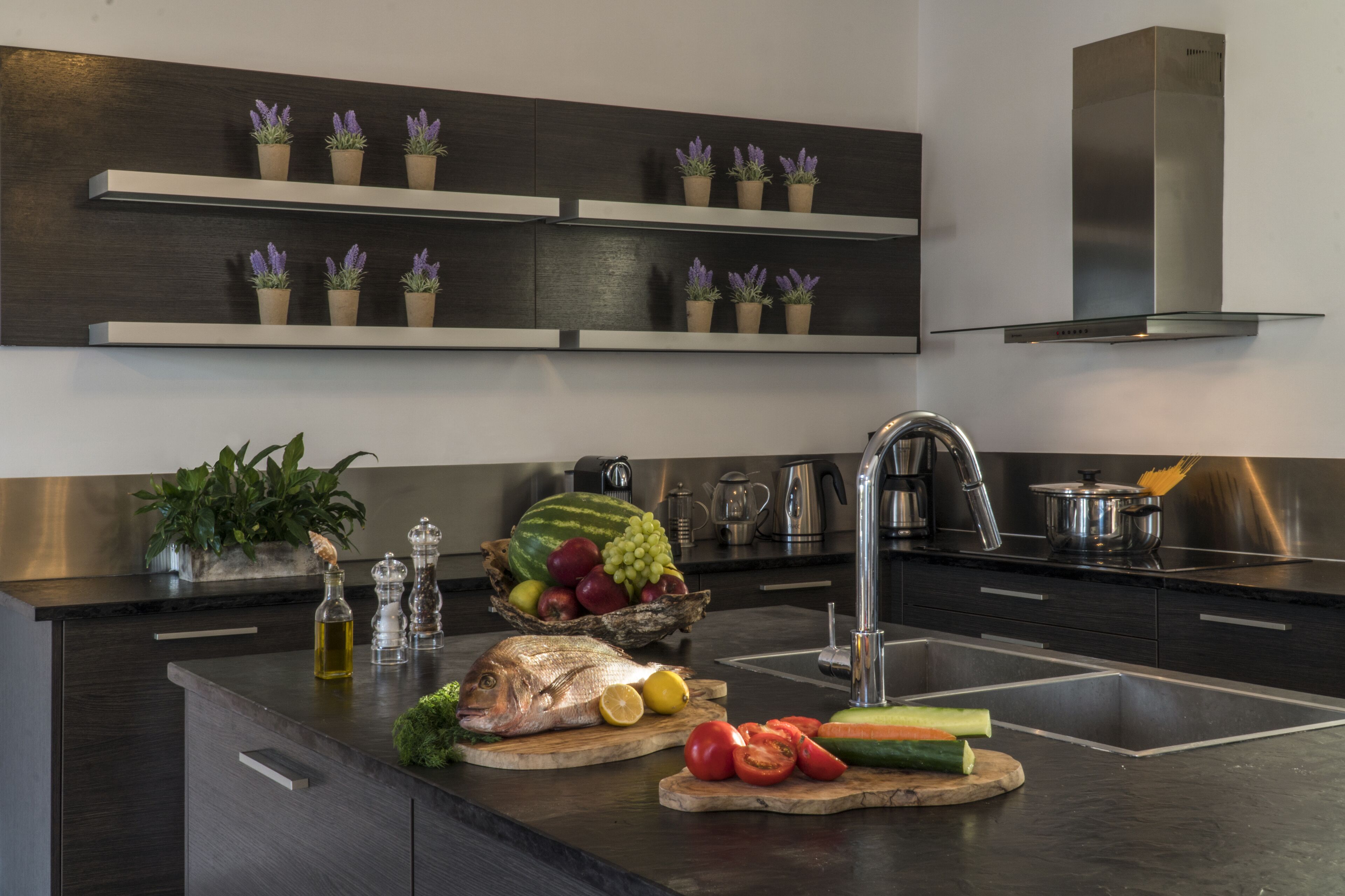 A modern kitchen with dark cabinetry, stainless steel appliances, and a central island with fresh produce and cooking utensils.