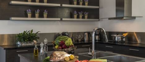 A modern kitchen with dark cabinetry, stainless steel appliances, and a central island with fresh produce and cooking utensils.
