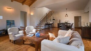 Un amplio salón con escalera de madera, muebles blancos y comedor.