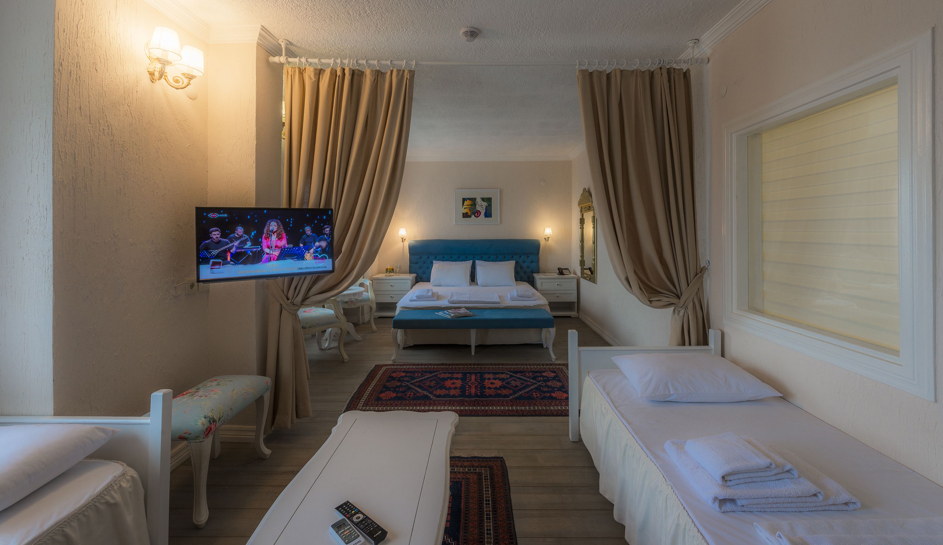 Una habitación de hotel con una cama, dos mesitas de noche, un televisor, una pequeña mesa y un banco.