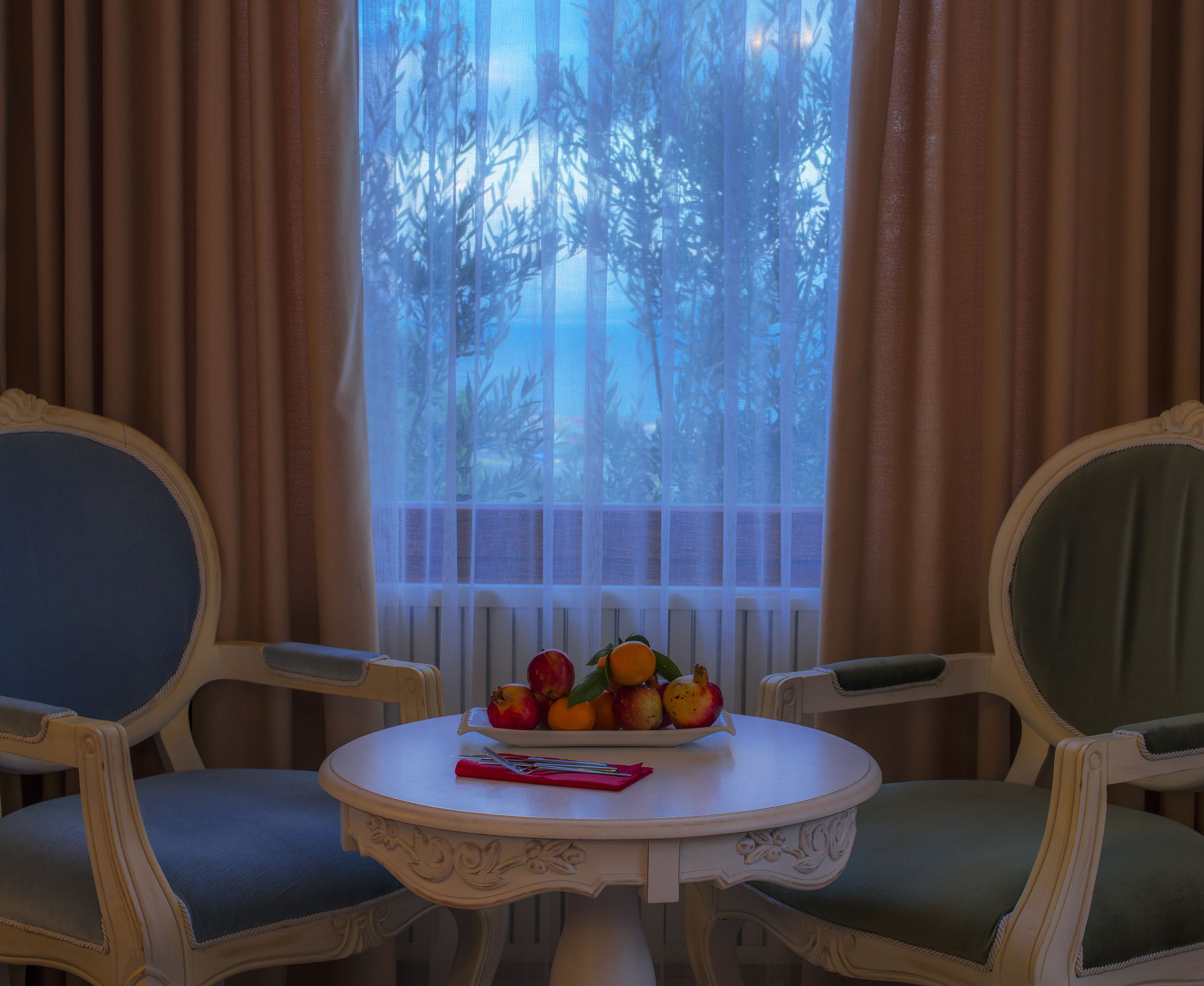 A dining area with a table set for two, featuring a fruit bowl and a red napkin.