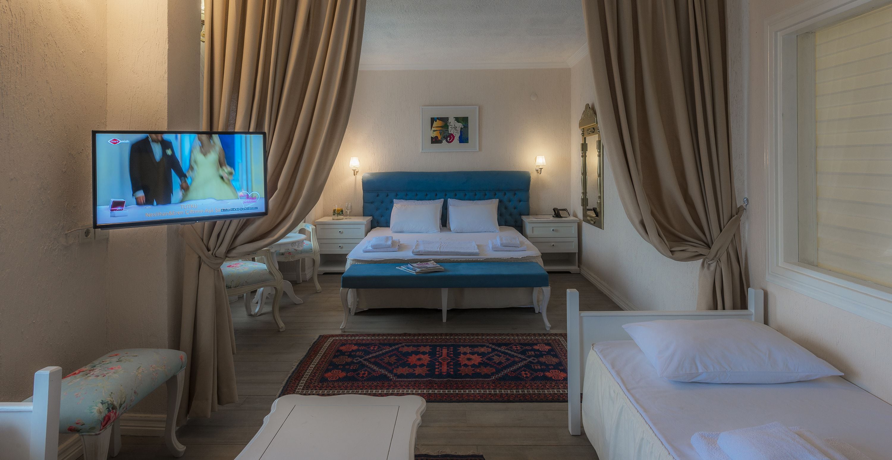 Habitación de hotel con una cama individual, una mesita de noche pequeña, una silla, un televisor montado en la pared y una ventana con cortinas.