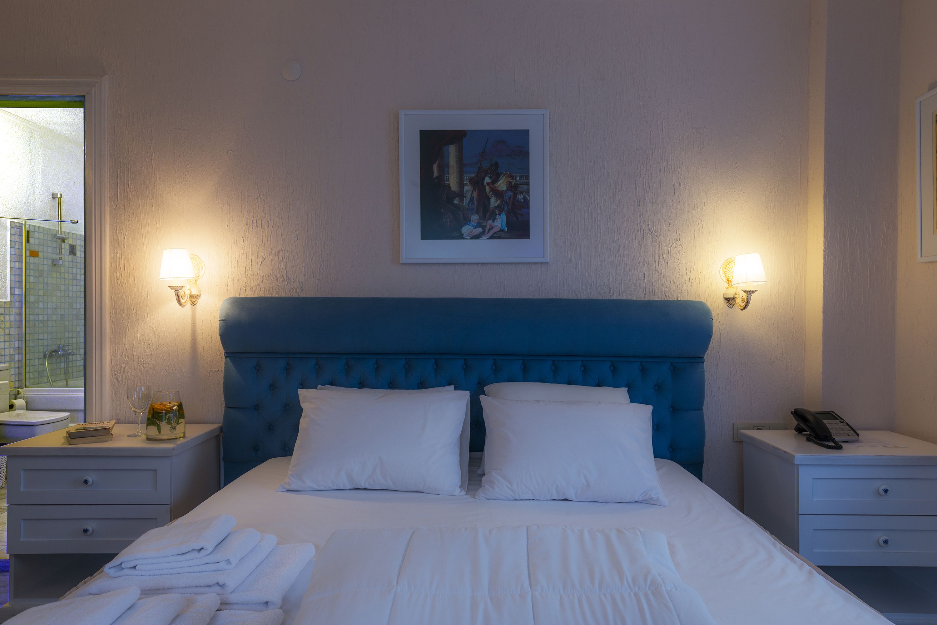 Habitación de hotel con una cama grande, dos mesitas de noche, un cuadro en la pared y una ventana con vistas.