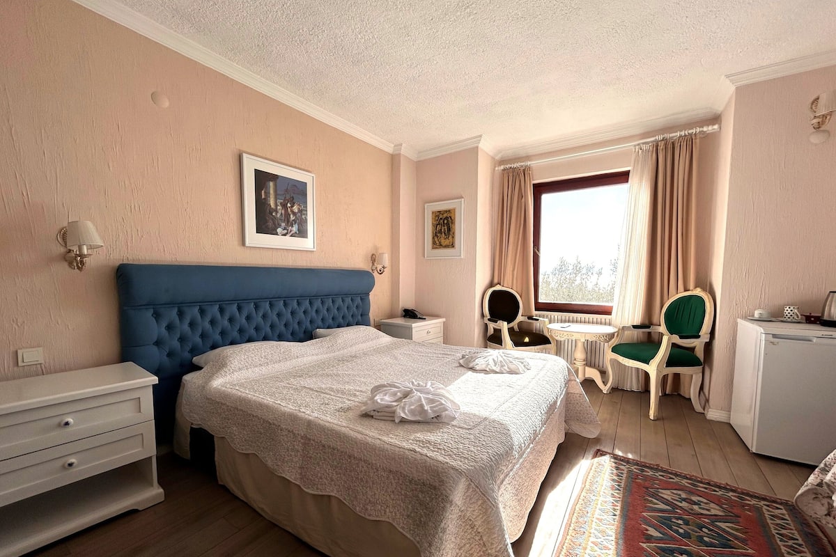 Una habitación de hotel con una cama grande, un escritorio, una silla, una mesita y una ventana con cortinas.