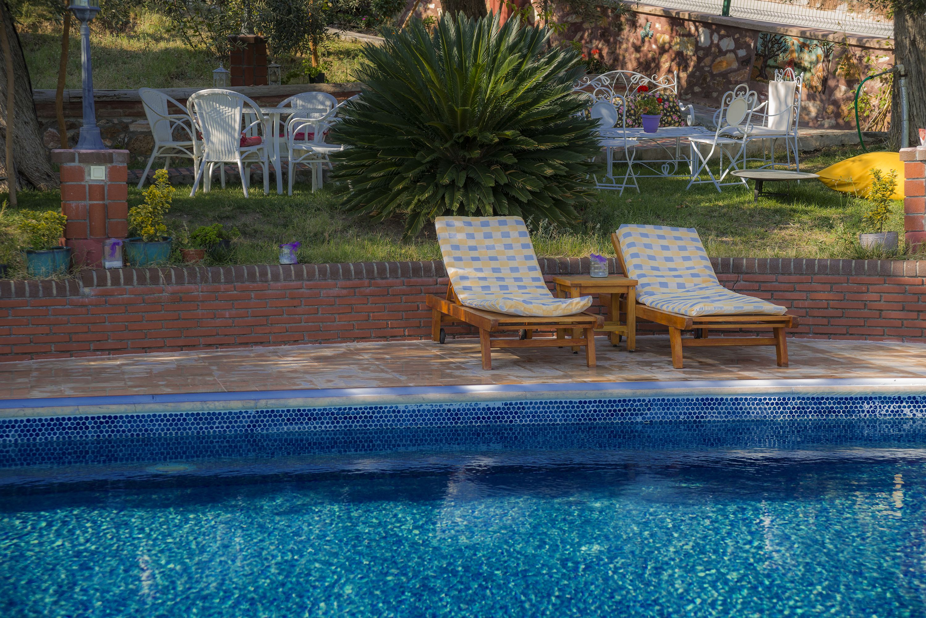 A pool area with two lounge chairs and a table, surrounded by a brick wall and potted plants.