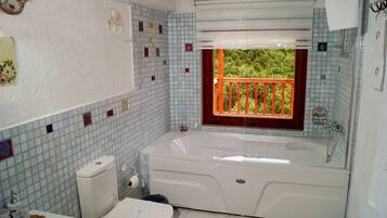 Un baño con bañera, inodoro y lavamanos. Se ve un ventanal con vistas a zonas verdes.