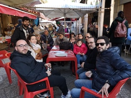 Un gruppo di persone sedute a un tavolo rosso con tovaglia bianca, sotto un tetto bianco.