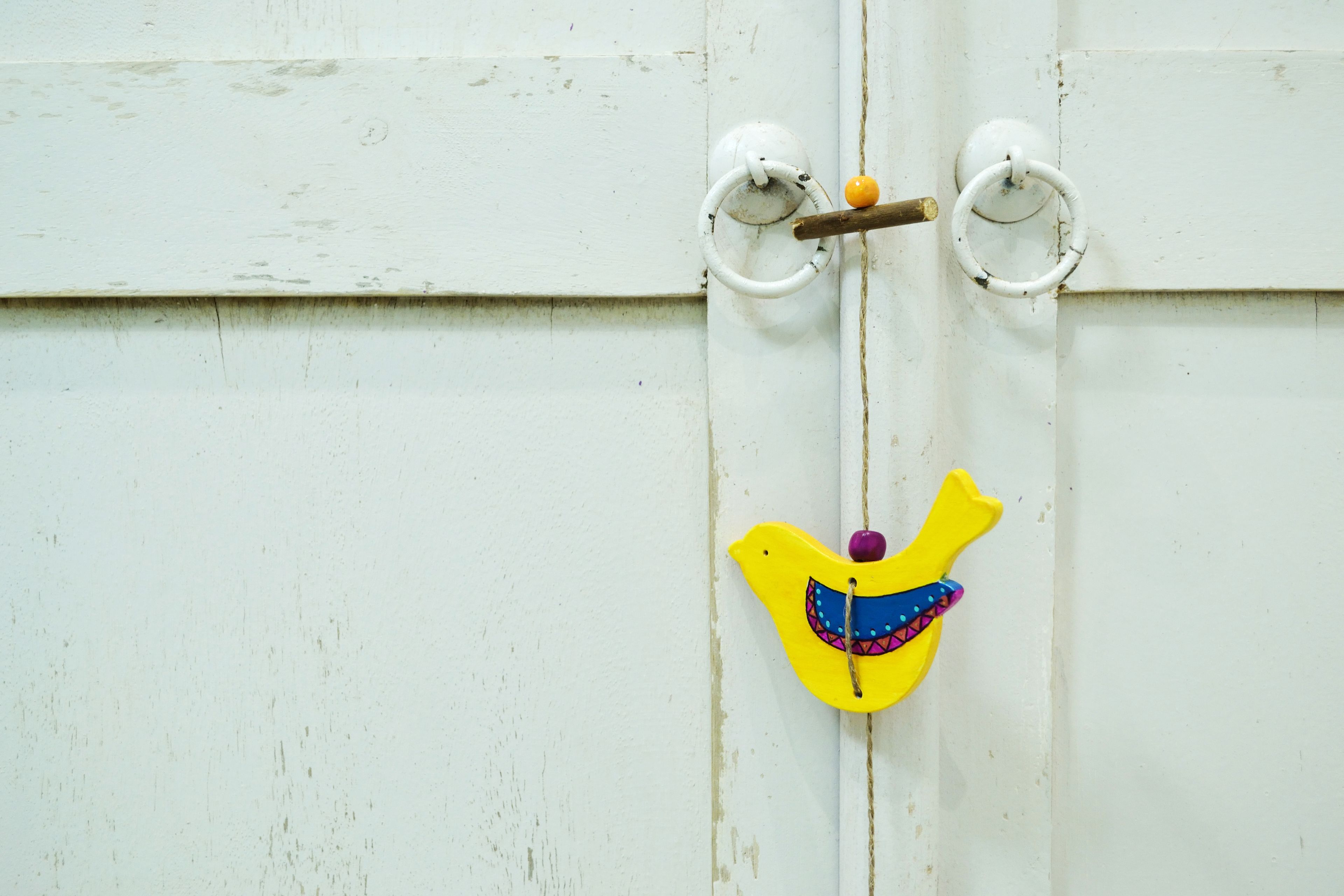 A white door with a yellow bird-shaped decoration hanging on a ring.