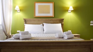A neatly made bed with white linens and towels, a wooden headboard, and two wall-mounted lamps on a green wall. - Piazza Marina (Palermo)