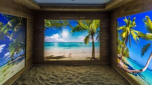 Ein Zimmer mit Wandgemälde vom Strand, sandigem Boden und Holzverkleidung.