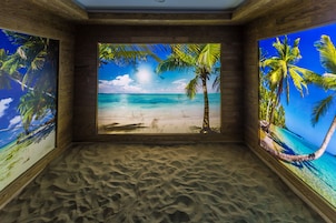 Una habitación con un mural de playa en las paredes, suelo de arena y paneles de madera.