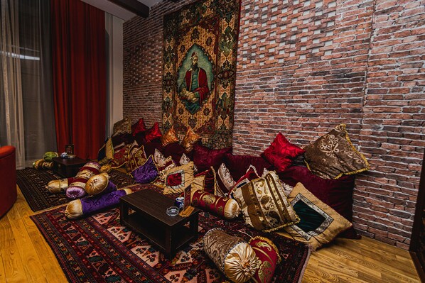 A room with a brick wall, a large tapestry, and a sofa with multiple cushions.