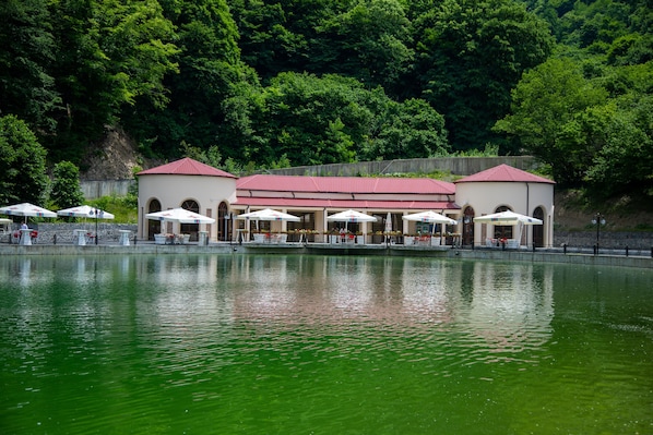 A lakeside building with outdoor seating and a red roof.