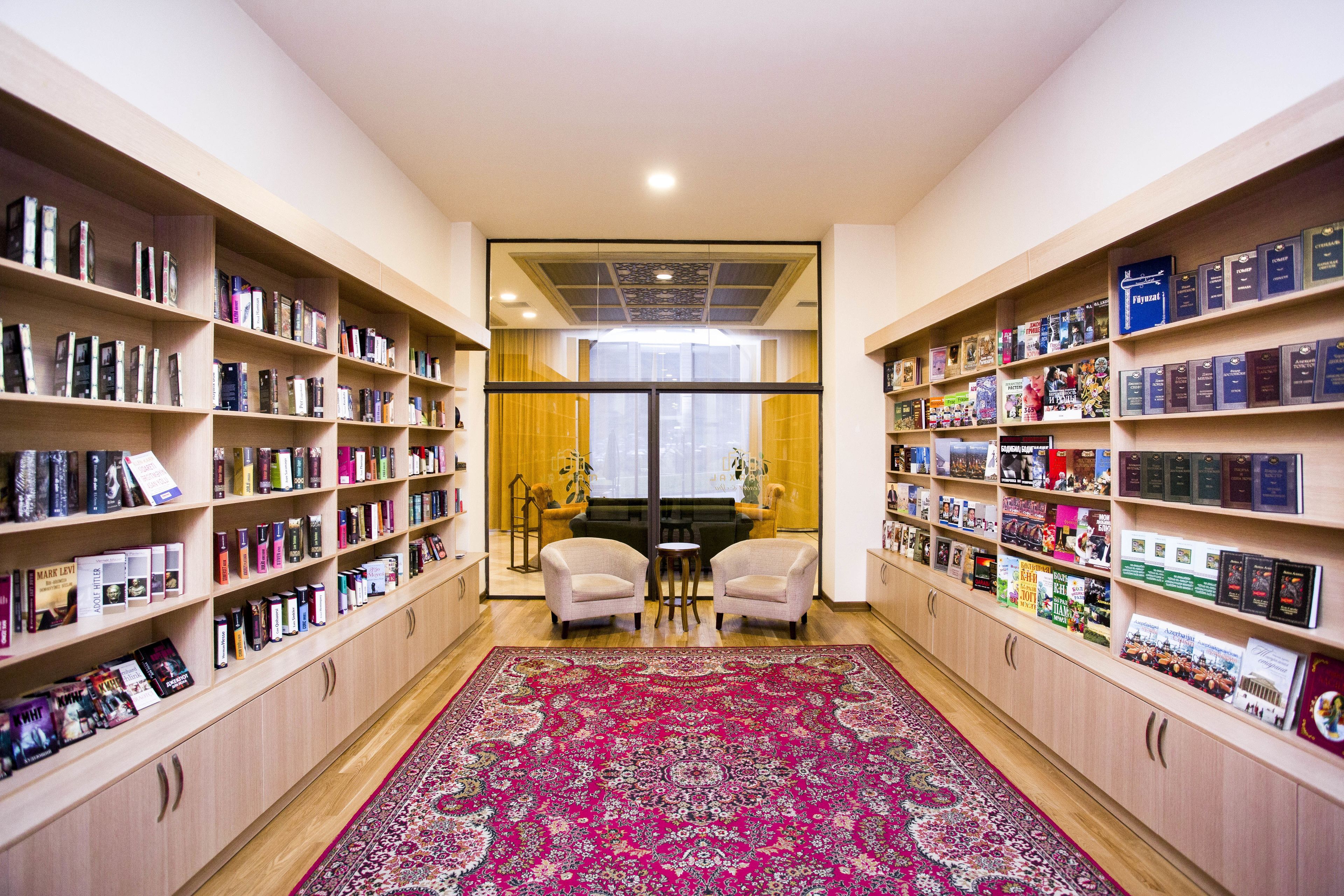 A library with bookshelves on both sides, a central seating area, and a large patterned rug.