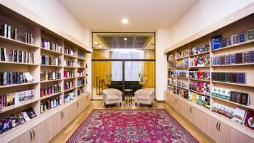 A library with bookshelves on both sides, a central seating area, and a large patterned rug.