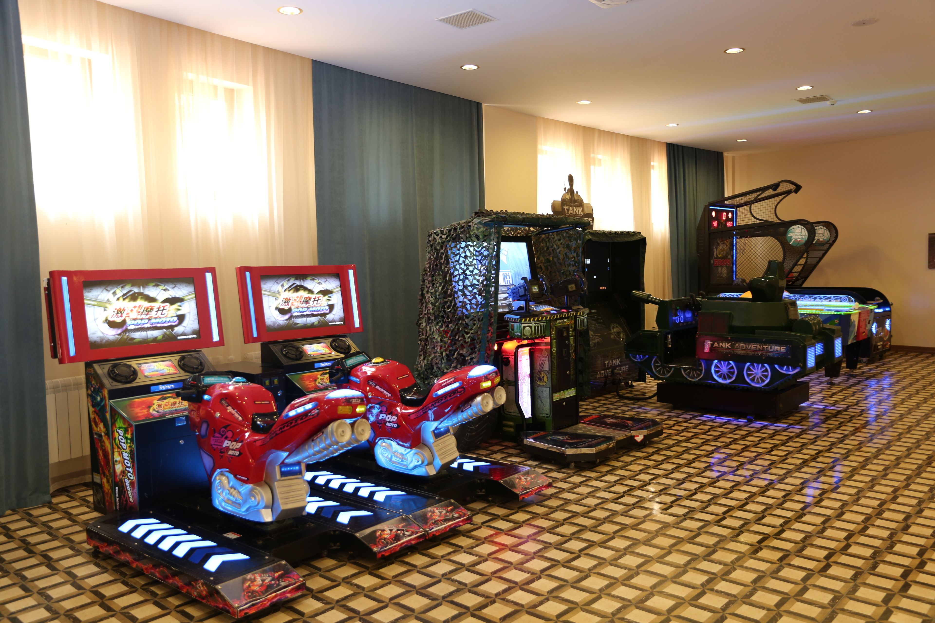 A gaming area with arcade machines, a tank-themed game, and two televisions displaying game screens.