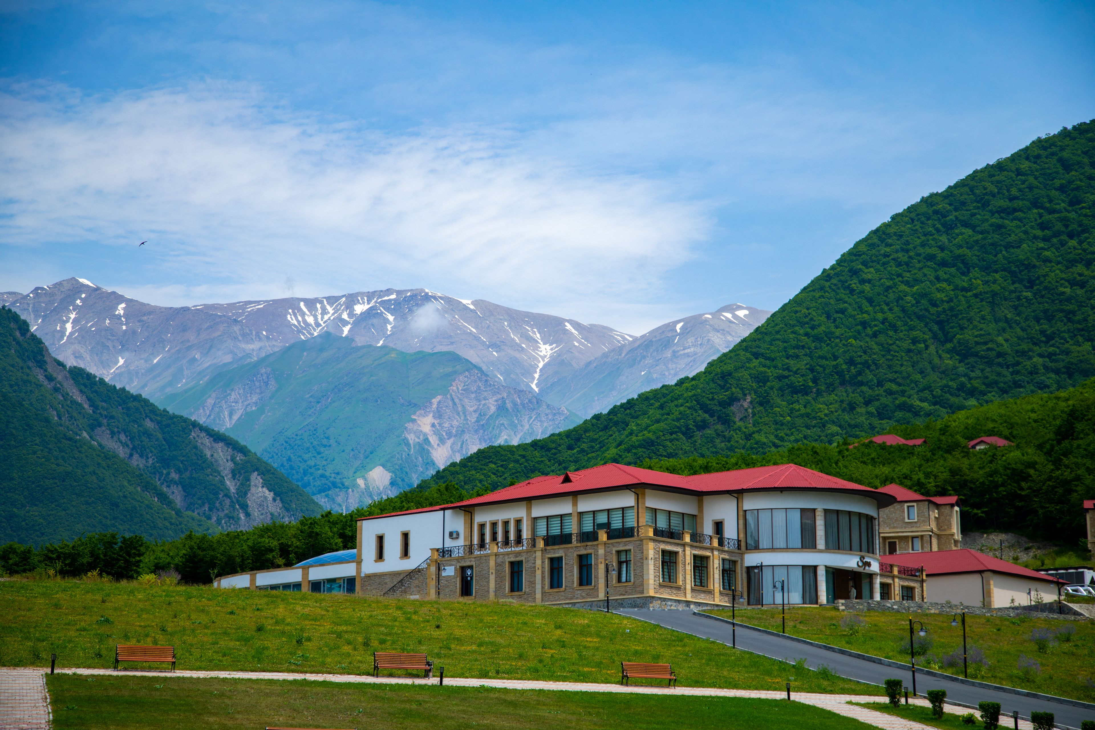 A building with multiple windows and a red roof, surrounded by green hills and mountains.