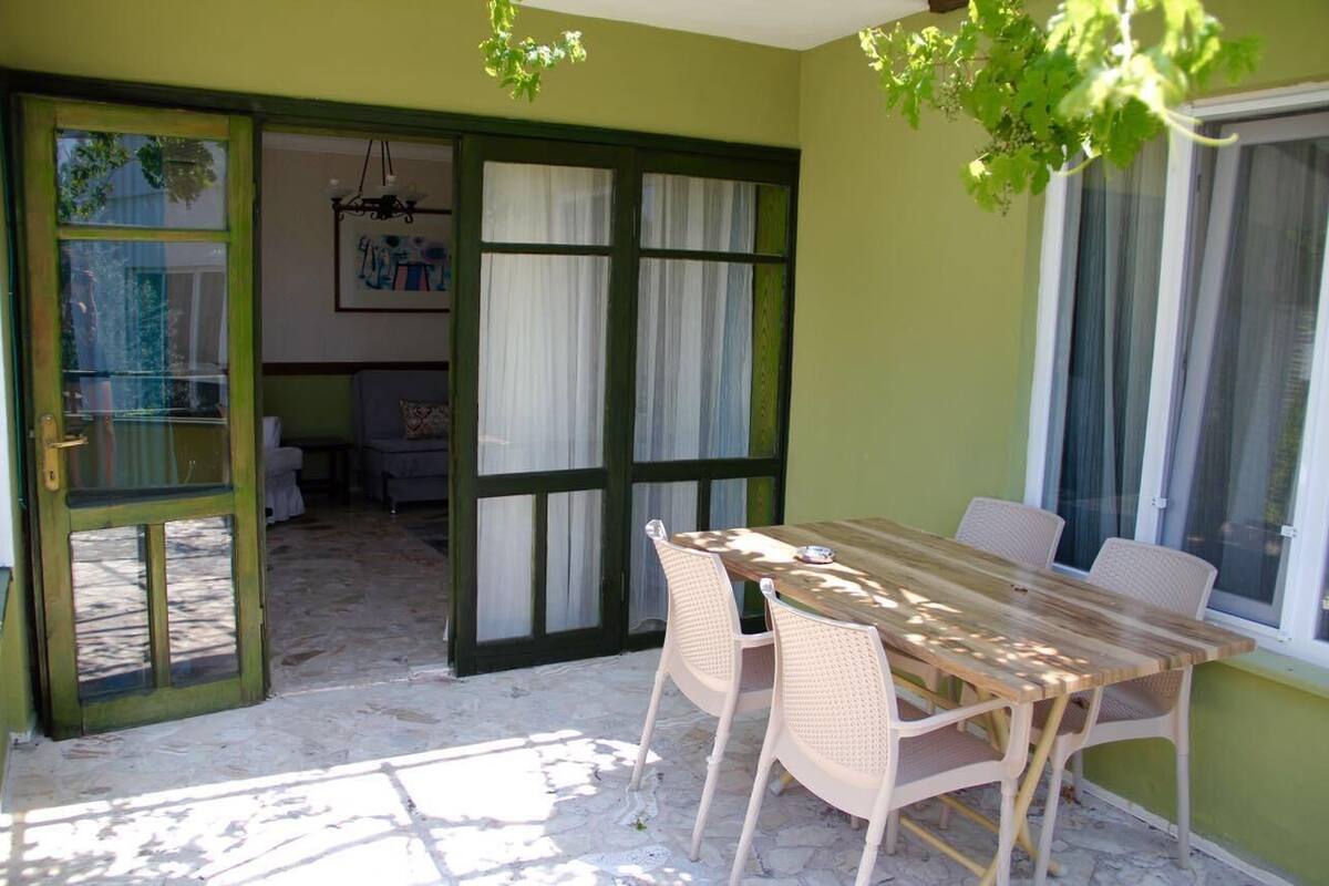 Una habitación con una mesa de madera, sillas de mimbre, una puerta verde y una ventana con cortinas.