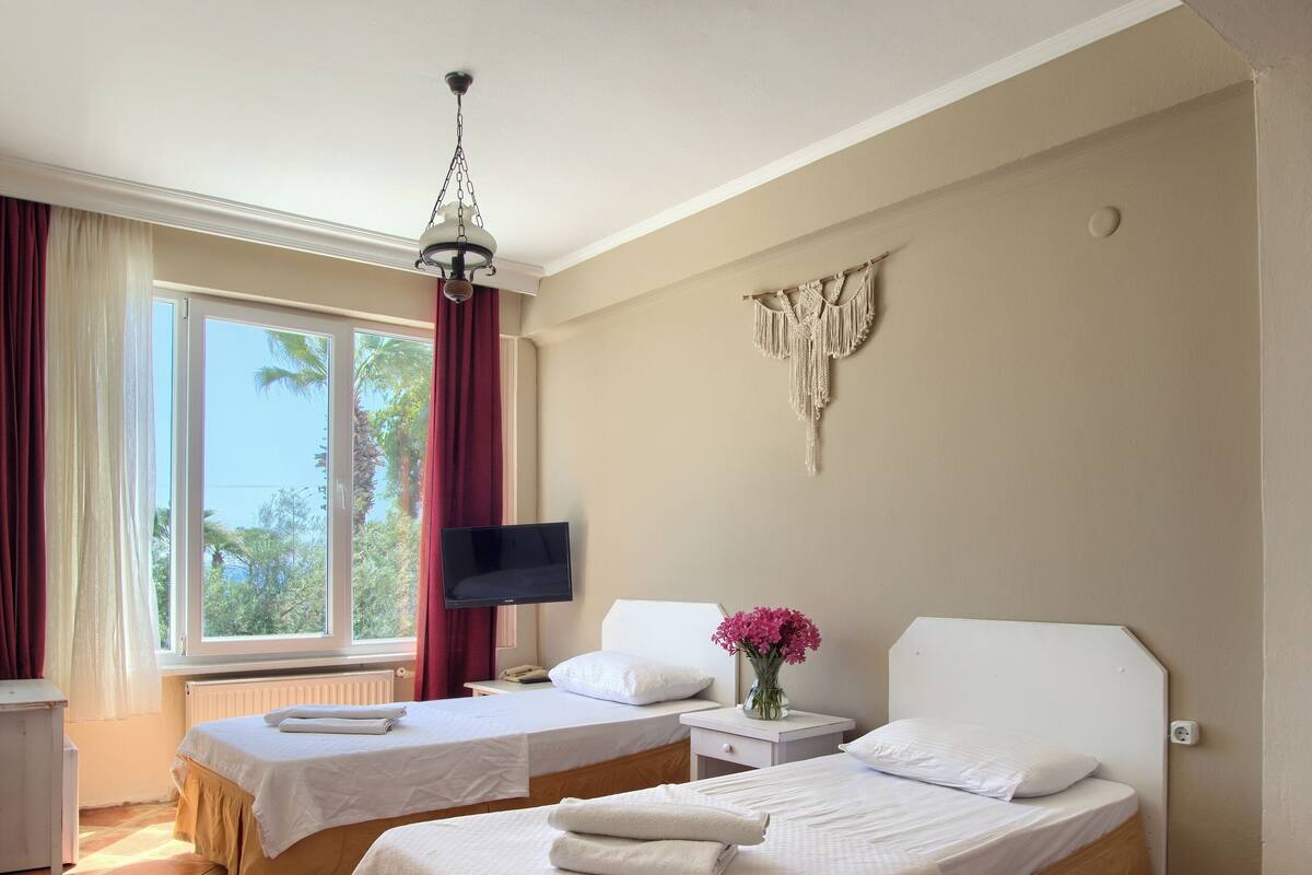 Habitación de hotel con dos camas, televisión, ventana con cortinas, decoración en la pared y suelo de baldosas.