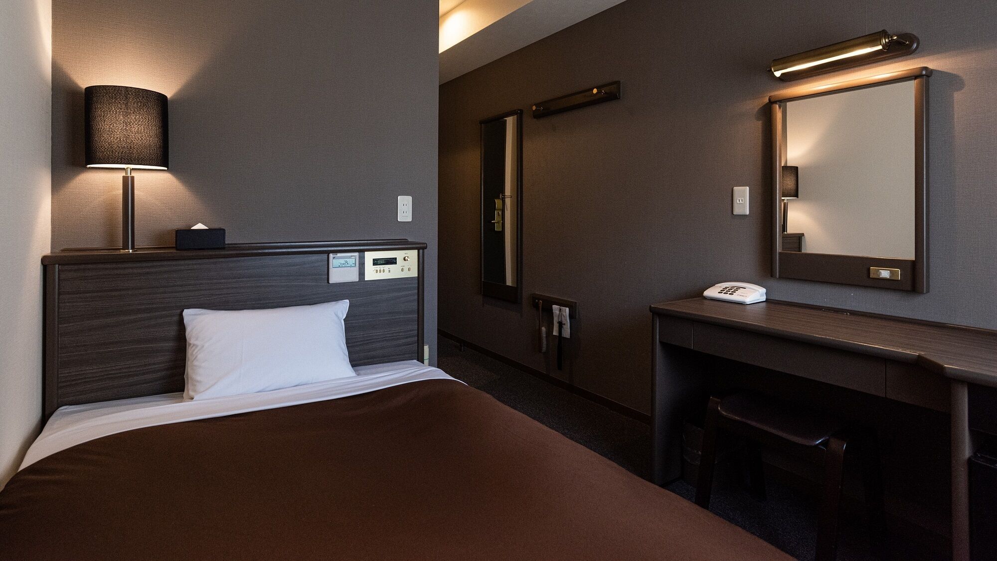 Une chambre d’hôtel équipée d’un lit, d’une table de chevet, d’une lampe, d’un miroir et d’un bureau avec un téléphone.