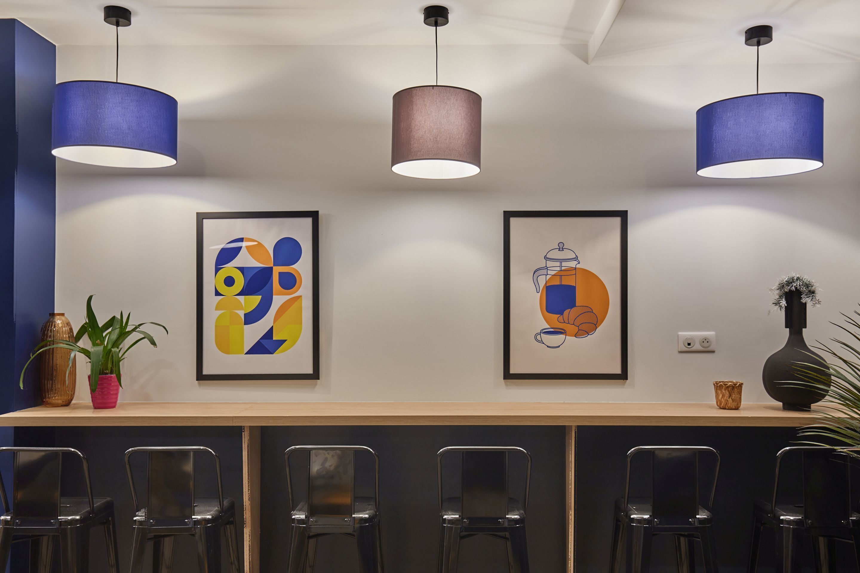 A modern bar area with a long counter, black chairs, and two pendant lights.