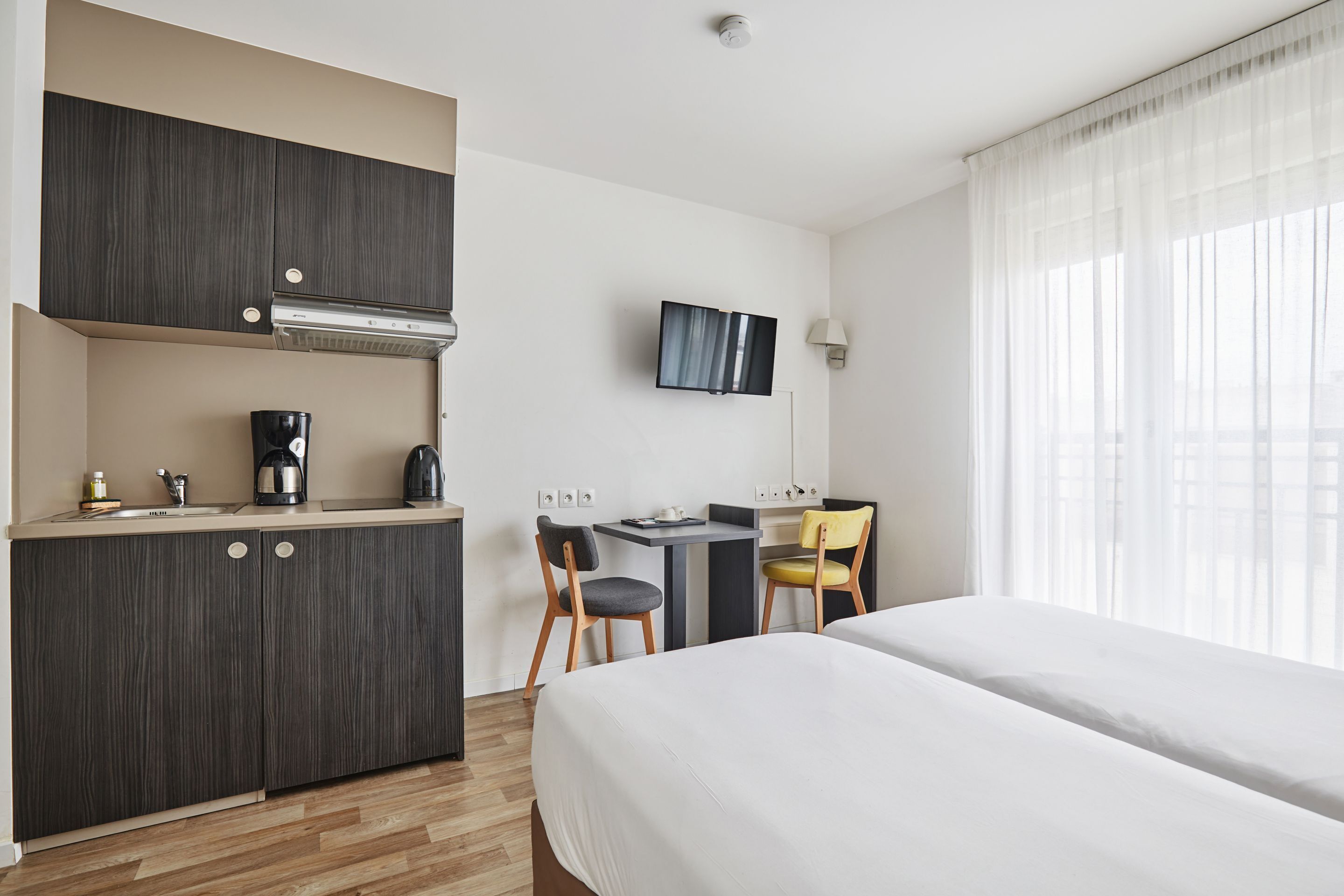 A hotel room with a bed, a desk, a chair, a TV, and a kitchenette.