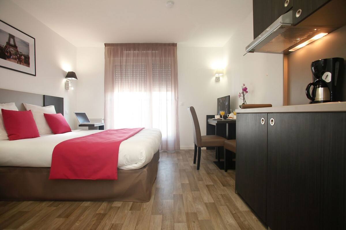 Een hotelkamer met een bed, een bureau, een koffiezetapparaat en uitzicht op de Eiffeltoren.