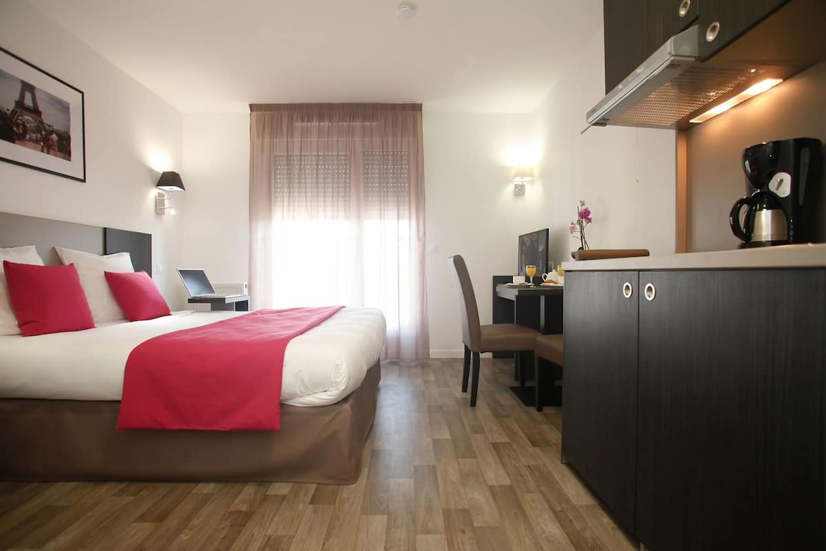 A hotel room with a bed, desk, and kitchenette.