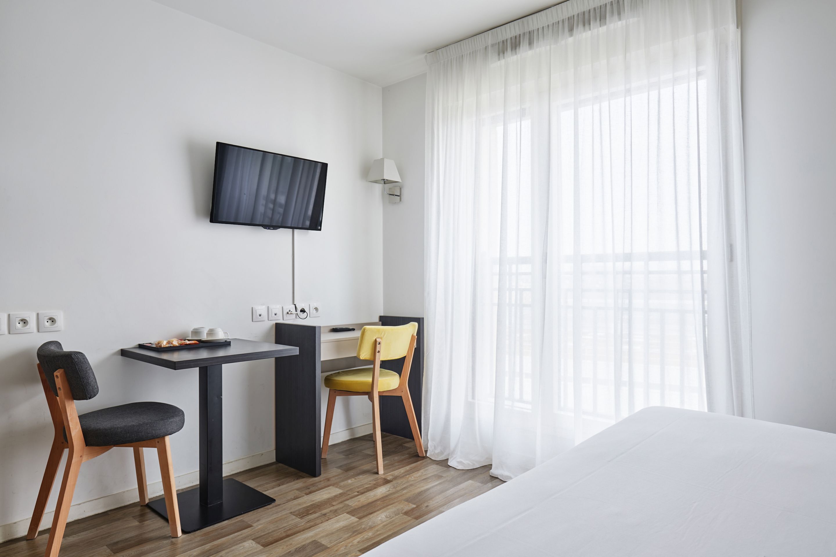 A hotel room with a bed, a desk with a chair, a television, and a window with curtains.