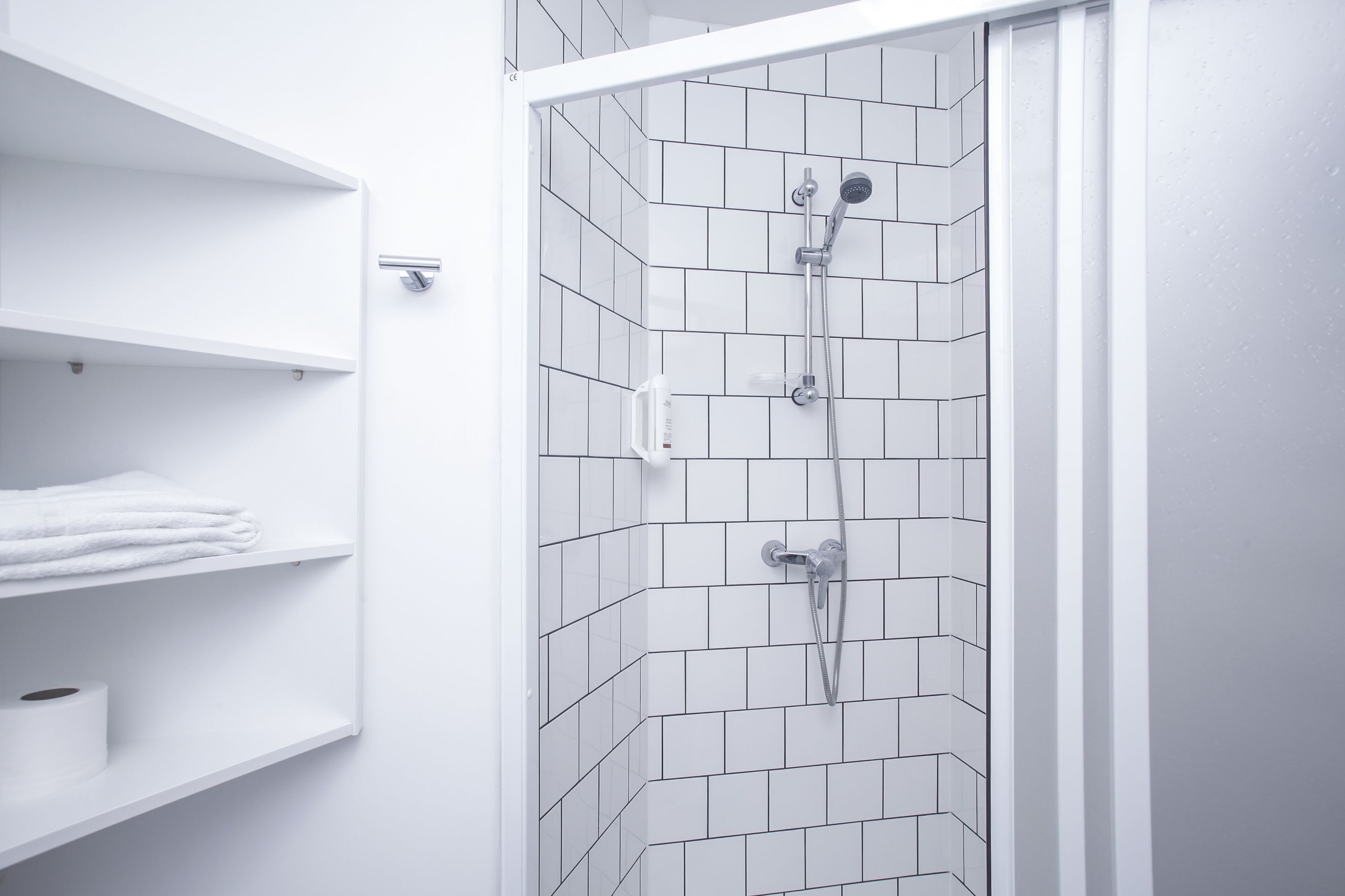 A shower with white tiled walls and a white door frame.