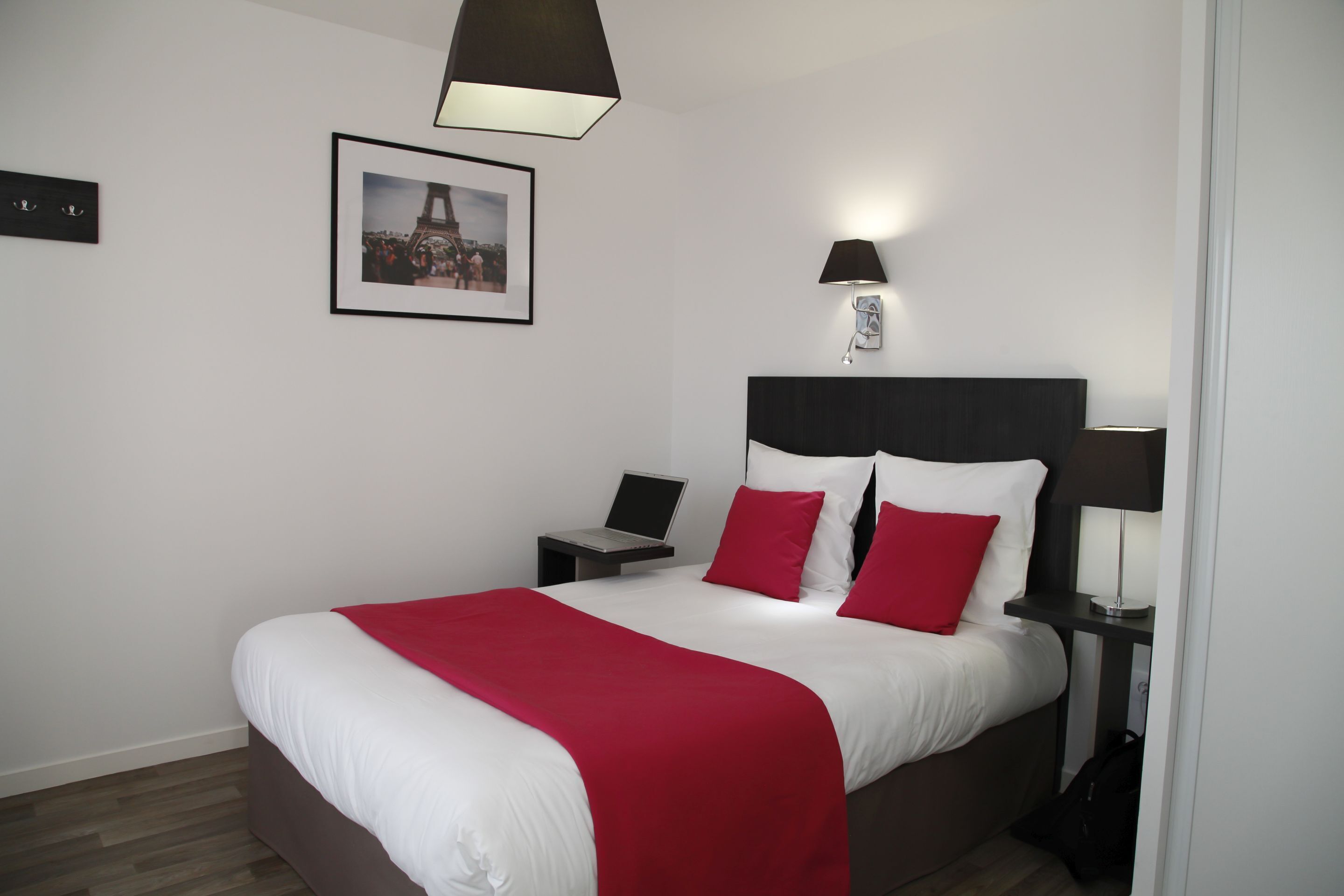 Ein modernes Hotelzimmer mit einem großen Bett, einem Schreibtisch, einem Stuhl, einer Lampe und einem gerahmten Bild an der Wand.